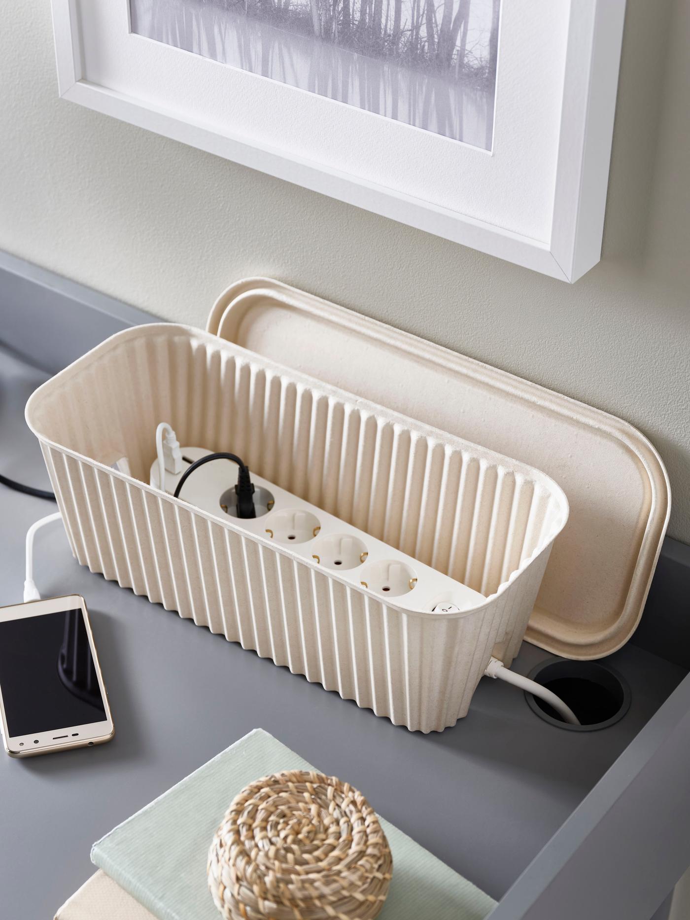 An IKEA HÖNSNÄT cable management box in beige on a grey desk