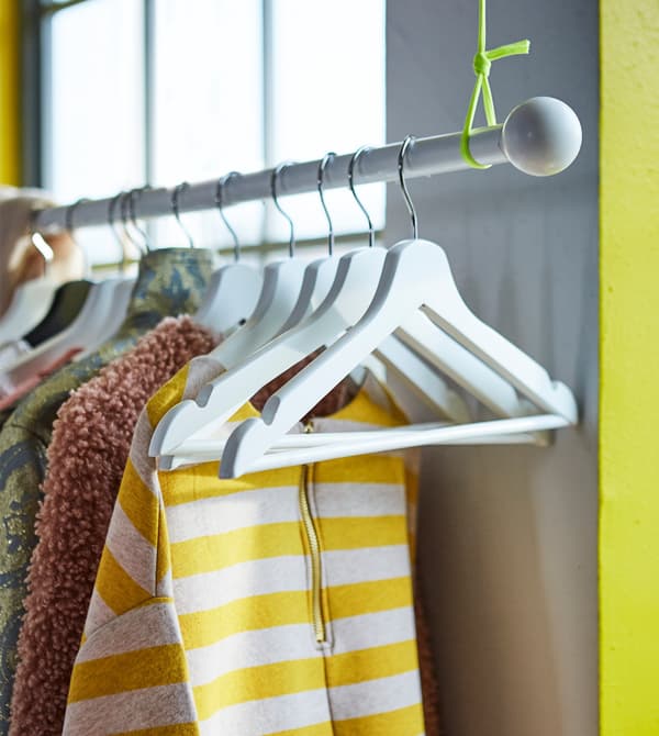 An IKEA HUGAD curtain rod suspended from the ceiling and used to hang clothes.