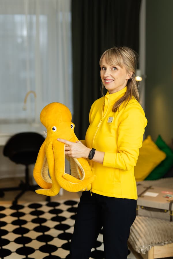 An IKEA Interior Designer in a yellow jacket smiles in camera and holds a yellow toy octopus.