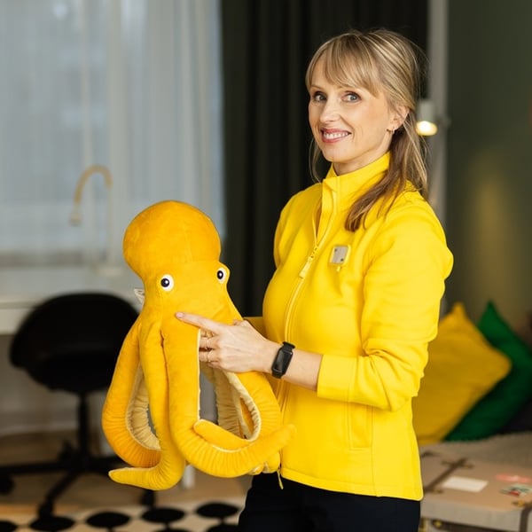 An IKEA Interior Designer in a yellow jacket smiles in camera and holds a yellow toy octopus.