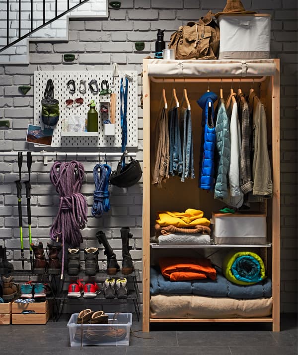 An IKEA IVAR shelving unit in solid pine with a rolled-up cover, and clothes on hangers and blankets inside.