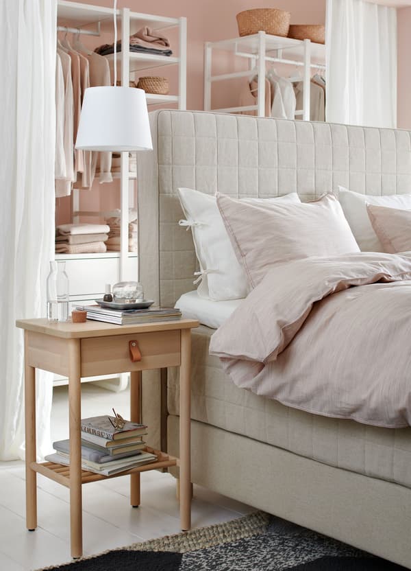 An IKEA JÄRA lampshade positioned above a bedside table next to a beige coloured divan bed.