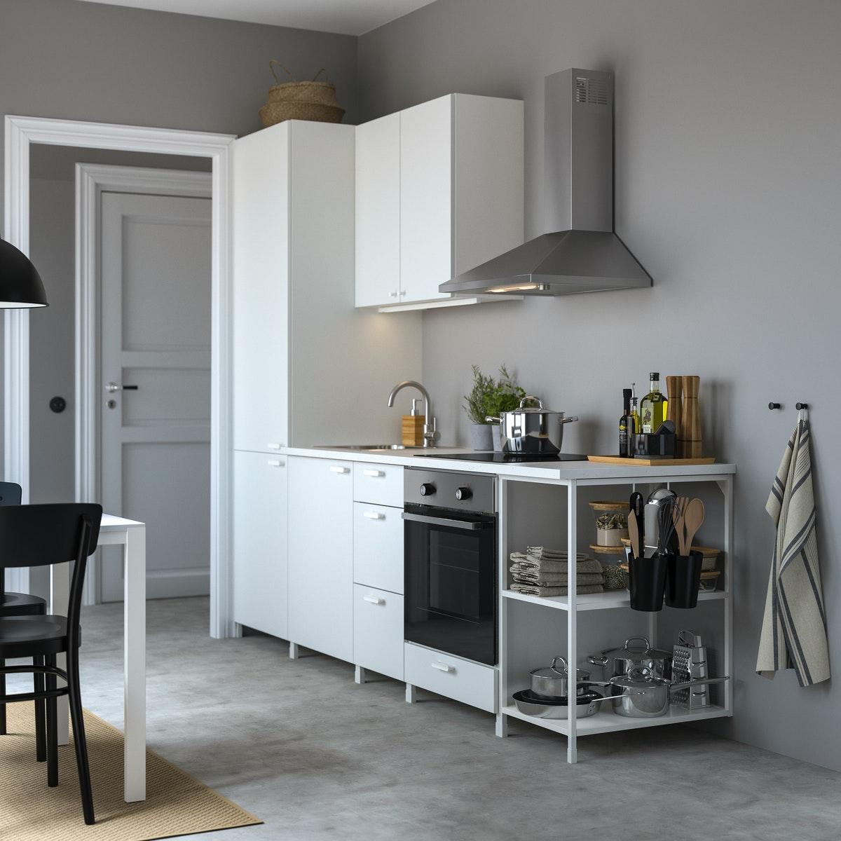 An IKEA kitchen with white cabinets, steel appliances in a kitchen with grey walls and grey floors.