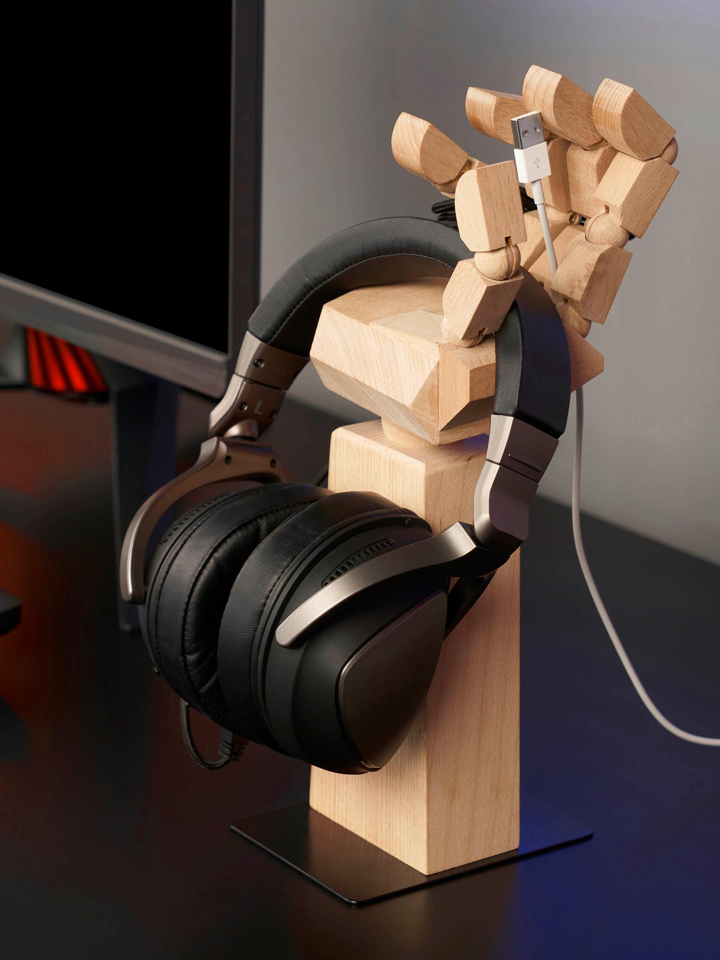 An IKEA LÅNESPELARE decorative wood hand holding a set of black headphones