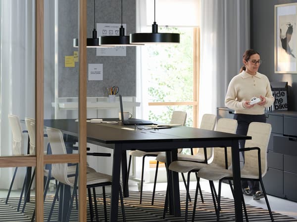 An IKEA MITTZON conference table in brown in a meeting room with beige chairs, a person walking alongside.