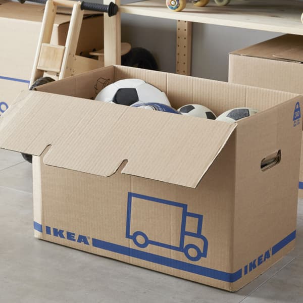 An IKEA moving box sitting on the ground with soccer balls inside.