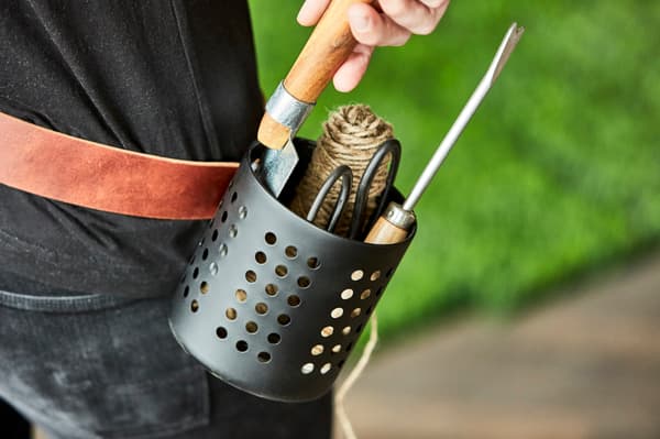 An IKEA ORDNING utensil holderturned into a gardening tool belt sits in the grass.
