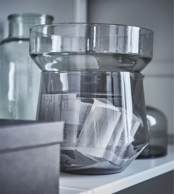 An IKEA PS 2017 transparent glass vase in gray with receipts inside.