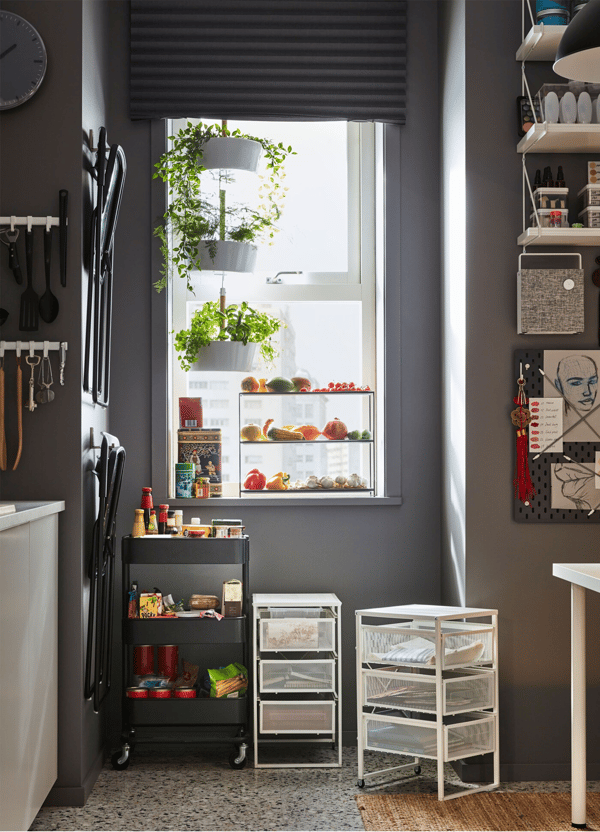 An IKEA RÅSKOG black trolley on wheels, beside 2 white LENNART drawer units, under a window in a home office space. 