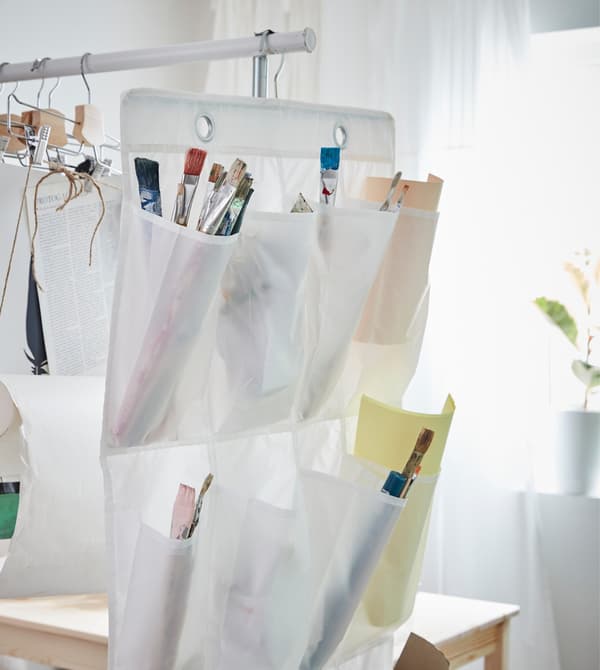 An IKEA SKUBB hanging shoe organiser is repurposed to hold paint brushes and art supplies.