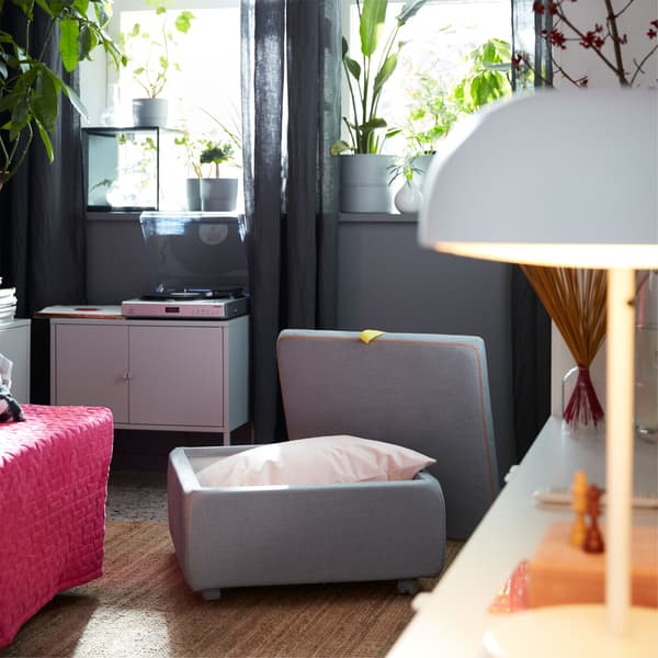 An IKEA SLÄKT light grey seat module, with castors and padded cushion, opened to reveal the storage space within.