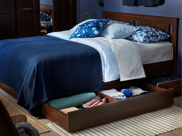 An IKEA SONGESAND brown bed frame, with blue bedlinen and spacious storage boxes under the bed, storing bedding and clothes.