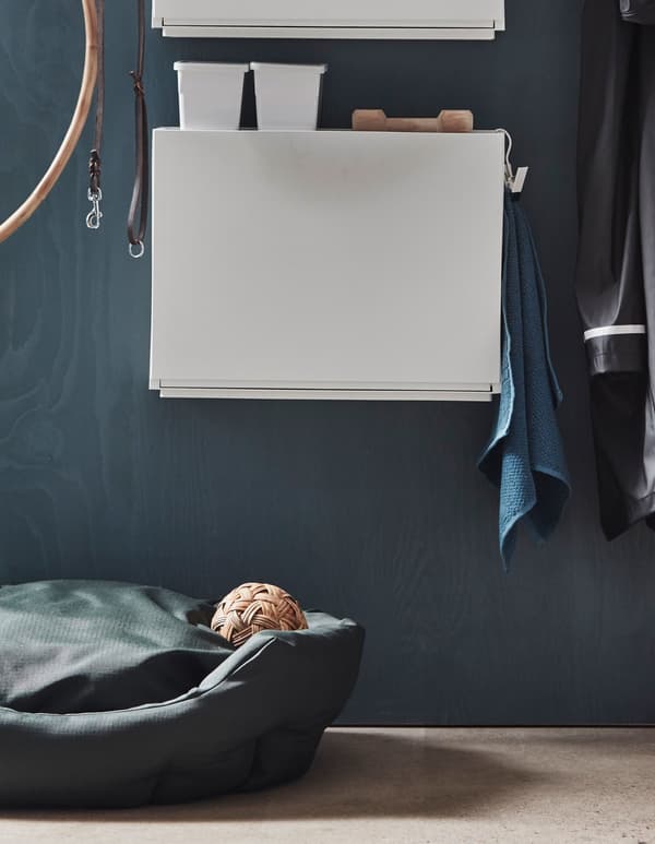 An IKEA TRONES shoe cabinet in a hallway stores dog accessories and is mounted above a dog bed.