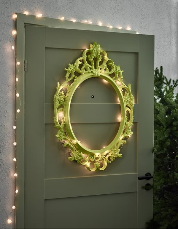 An IKEA UNG DRILL mirror frame spray painted green and wrapped with fairy lights as a door deco piece.