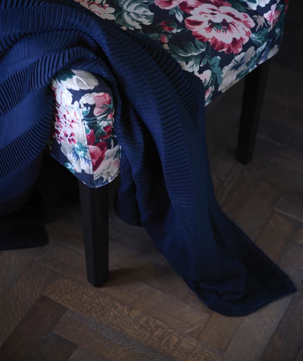 An IKEA VÄGMÅLLA dark blue throw draped on a floral patterned chair.