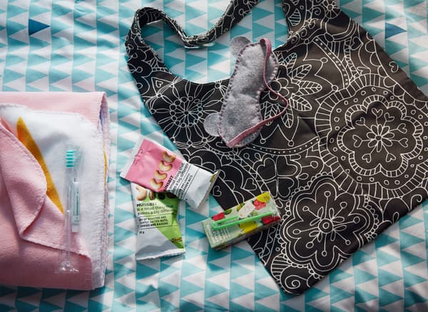 An IKEA VÄNSKAPLIG floral patterned bag with snacks, juice boxes, and a sleeping mask laying beside it.