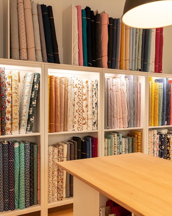 An illuminated shelf with many different bales of fabric in it.