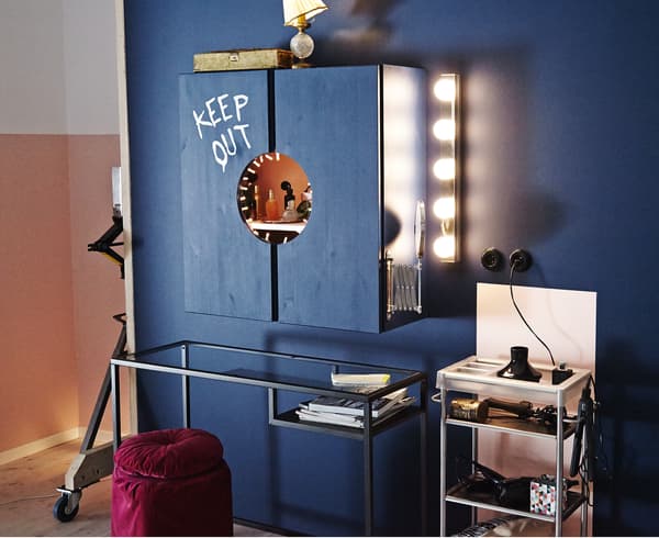 An image of a vanity station that consists of a cabinet, a small table and a place for the bathroom cart. The walls and cabinet are painted dark blue.