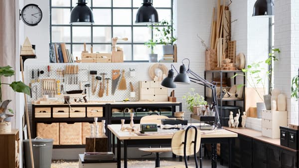 An industrial-style studio at home with high ceilings, furniture made from wood and black metal, and big windows.