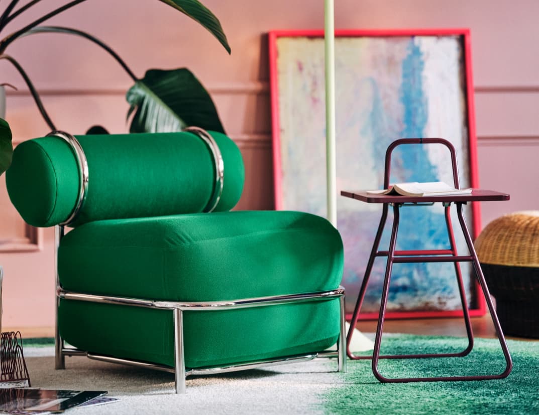 An inflatable green chair with chrome rims on a green and white rug. The cozy room also features a plant behind it and a side table with a book on top.