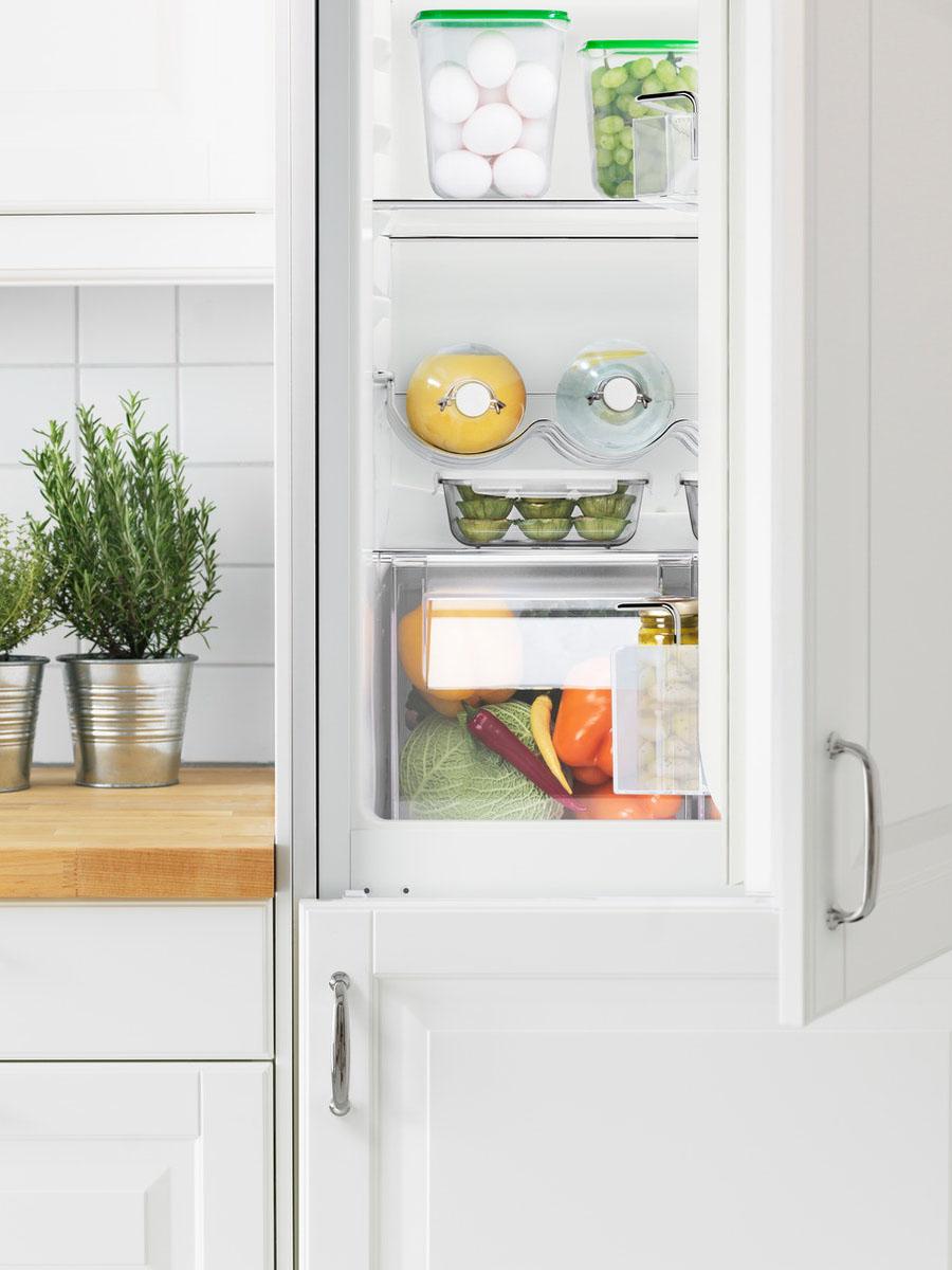An integrated fridge-freezer half open showing the internal organisation, in a white bright kitchen.