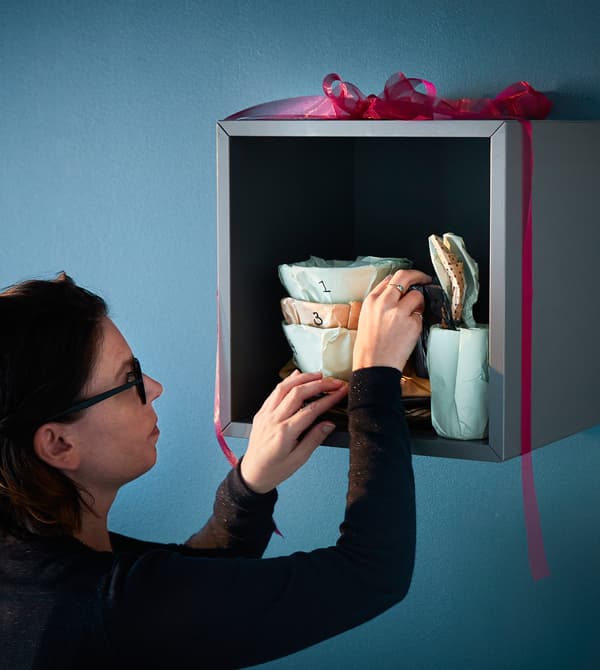 An interior designer arranges wrapped dinnerware on a shelf.