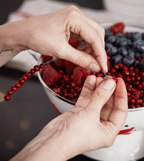 An interior designer is making a small wreath by threading lingonberries on steel wire.
