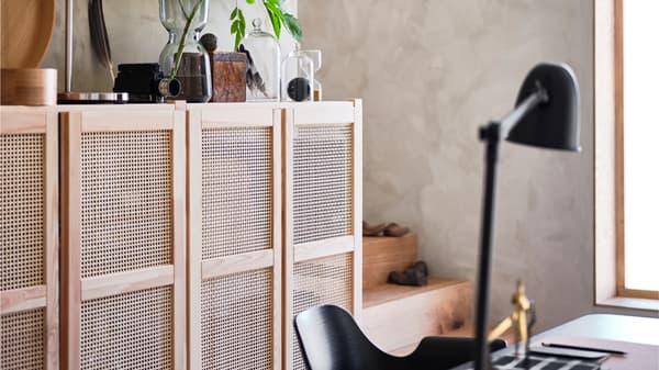 An IVAR cabinet with rattan doors with personal objects on its top. A chair sits in front of it.