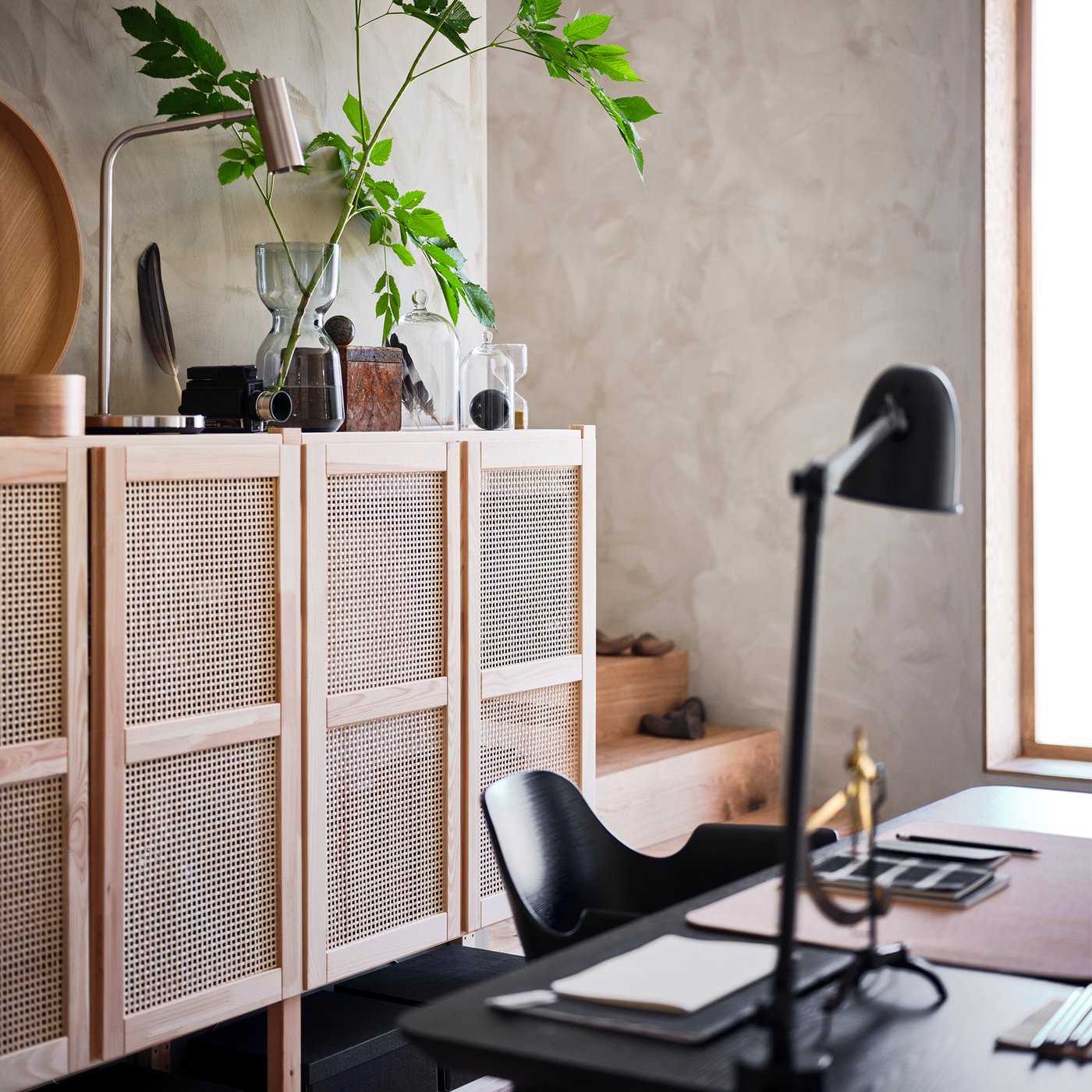 An IVAR cabinet with rattan doors with personal objects on its top. A chair sits in front of it.