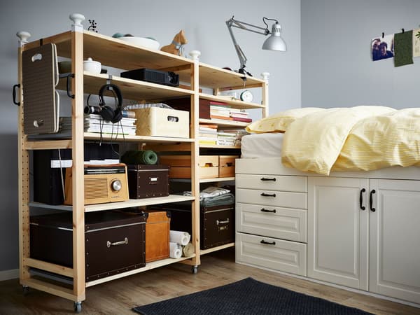 An IVAR shelf on wheels with storage boxes helps organize this small bedroom for a couple.