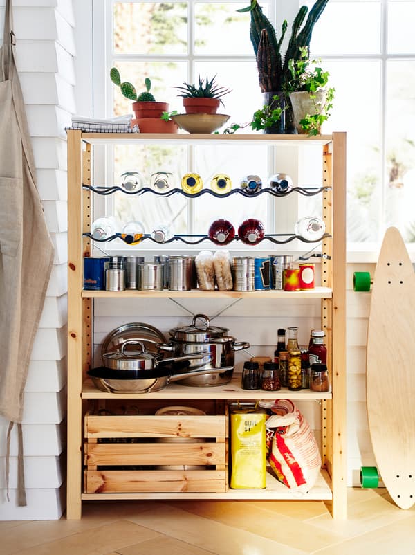 An IVAR unit stands by a window, organised as a small pantry with pots, dry goods, canned food, and bottles on racks.