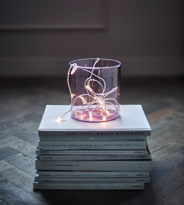 An LED lighting chain in a clear vase sitting on a stack of magazines.