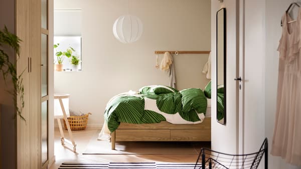 An oak veneer TONSTAD bed with storage with KUNGSCISSUS bed linen stands in a bedroom with racks with knobs on one wall.