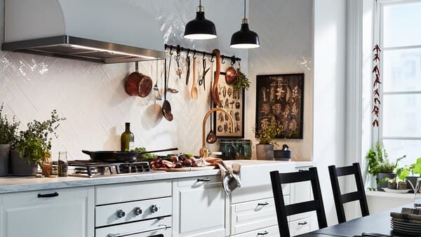 An off-white kitchen with traditional BODBYN doors and drawer fronts is illuminated by two black pendant lamps.