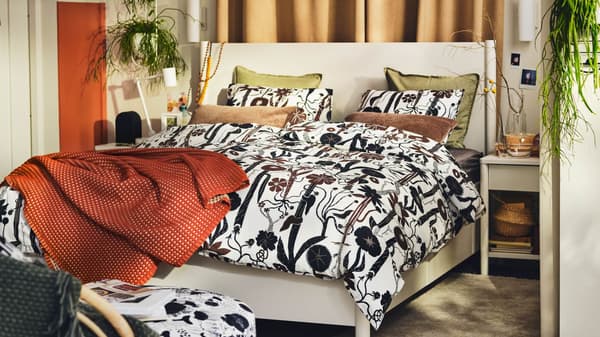 An off-white TONSTAD bed in a bright bedroom covered with white/black/brown LUNDSKAFTING bed linen and a rust throw.