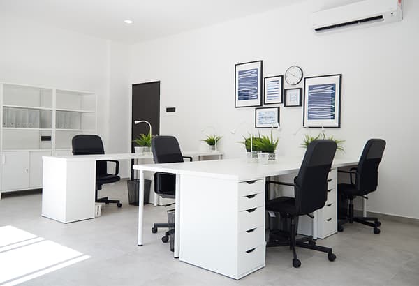 An offic area featuring white desks with drawers and black office chairs.