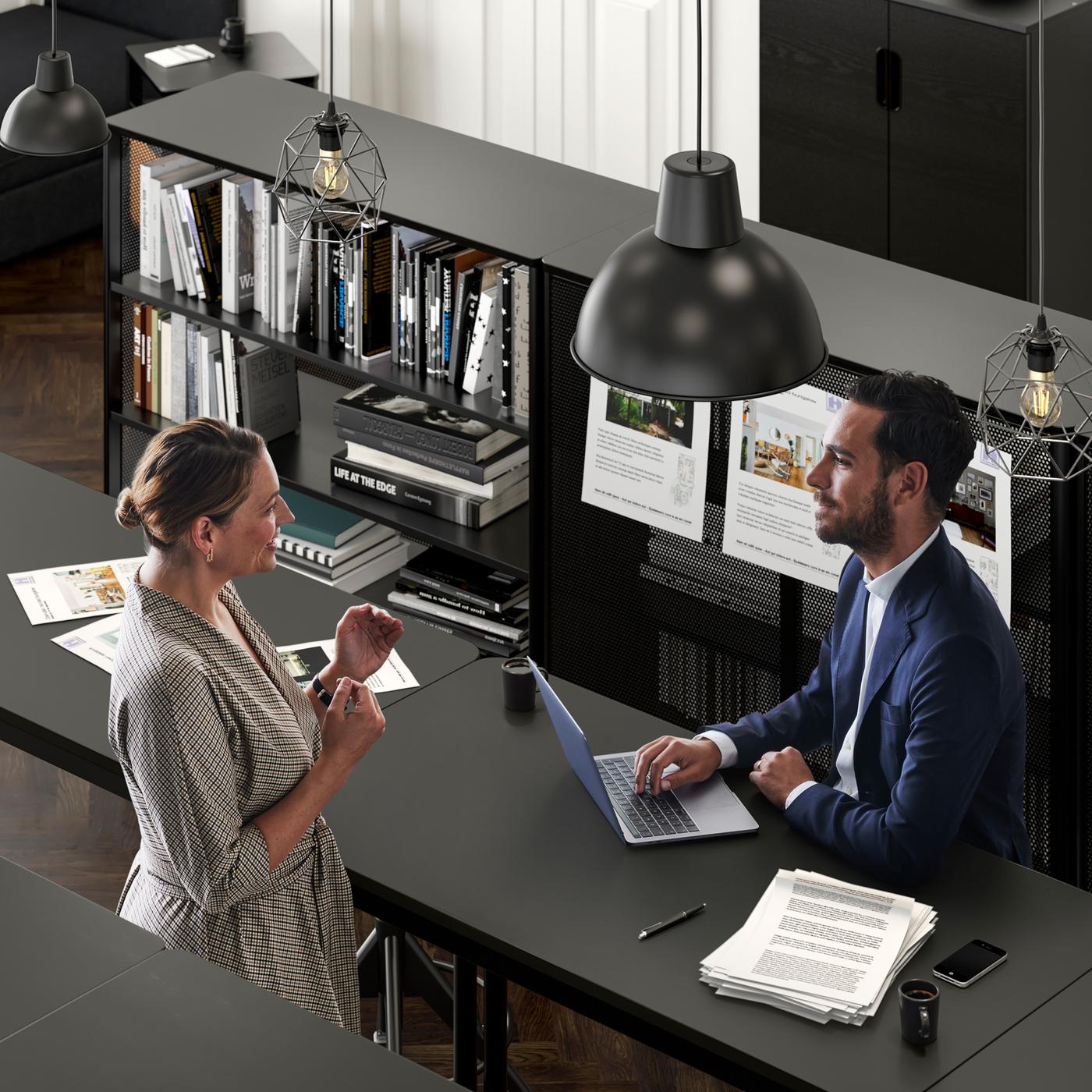 An office setting where a woman talks to a man in a suit who sits with his laptop by a TOMMARYD table.