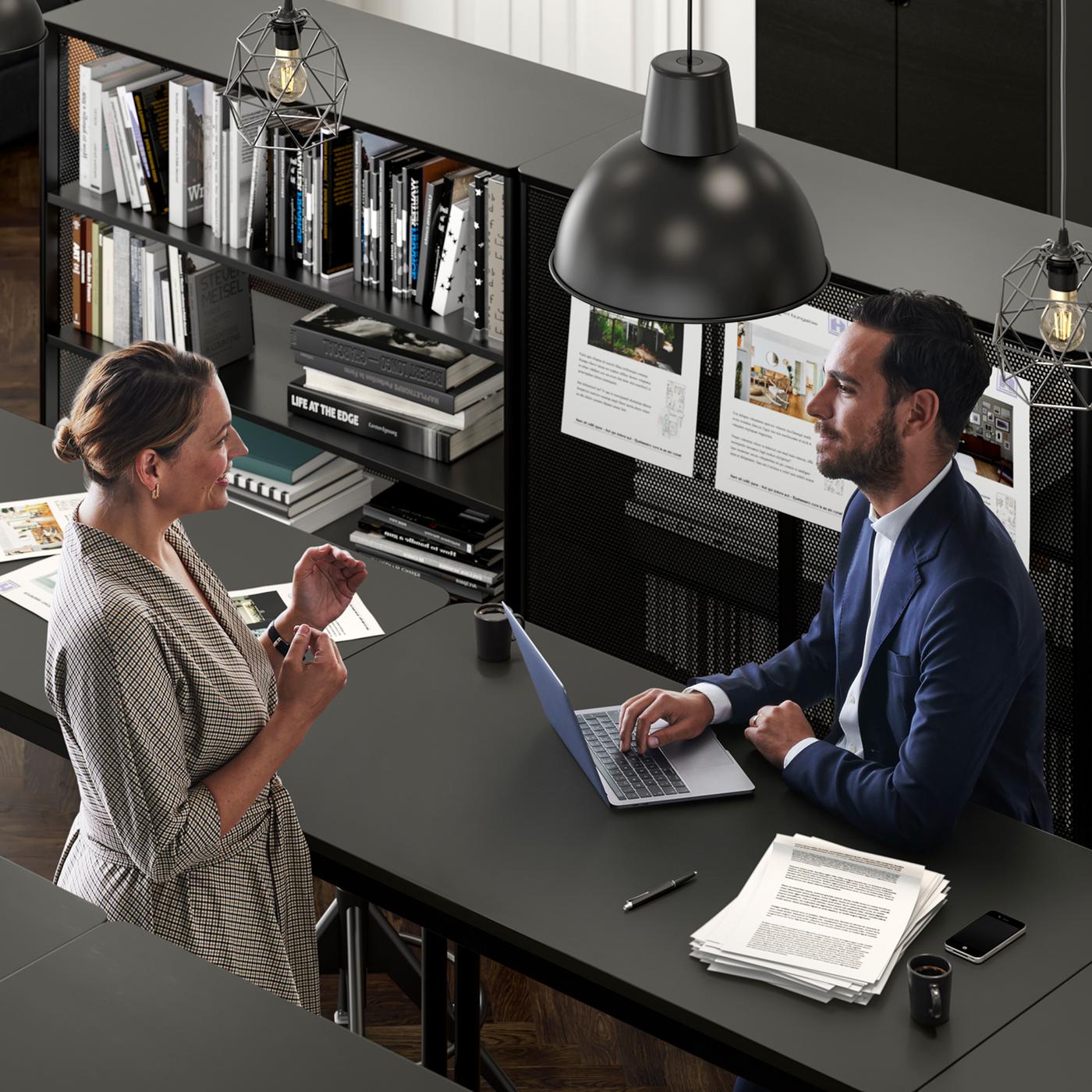 An office setting where a woman talks to a man in a suit who sits with his laptop by a TOMMARYD table.