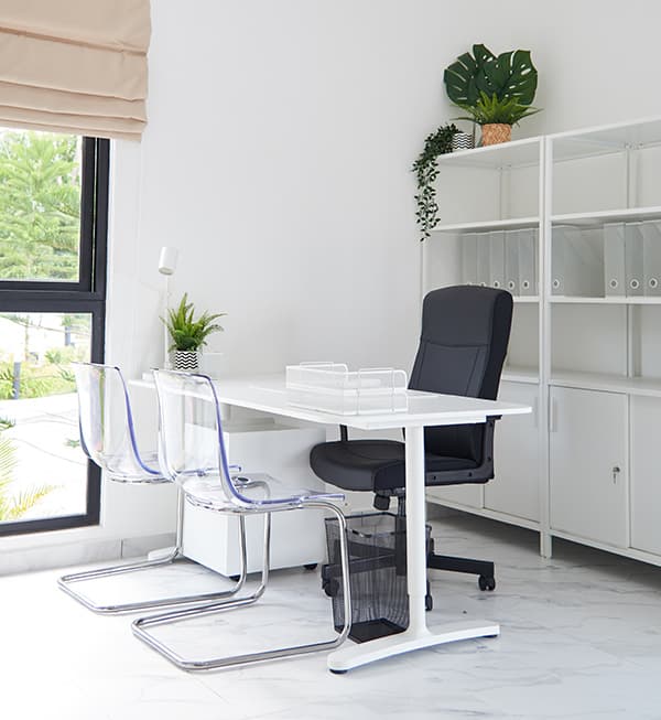 An office setting with a white desk, a black office and two transparent chairs.