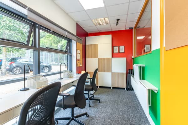 An office with multi-colour walls and beige desks and black desk chairs. 