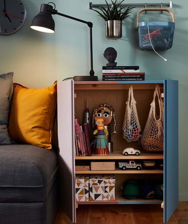An open cabinet in a living room revealing two net bags, several small boxes and toys.