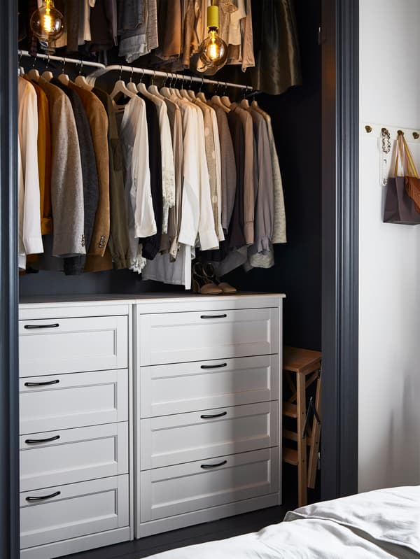 An open closet, in a nook, with two white chests of drawers and two rows of hanging clothes.
