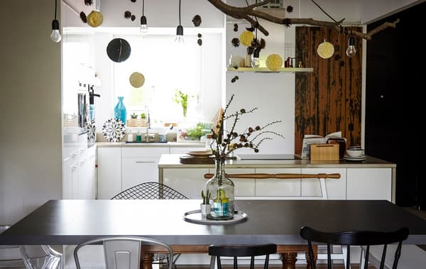 An open dining and kitchen space, with a black dining table, and light bulbs and paper decorations hanging from the ceiling.