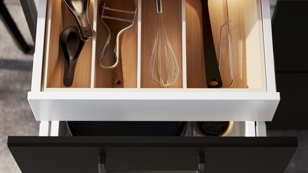 An open drawer with an UPPDATERA cutlery tray holding a potato peeler, a whisk and various other kitchen utensils.