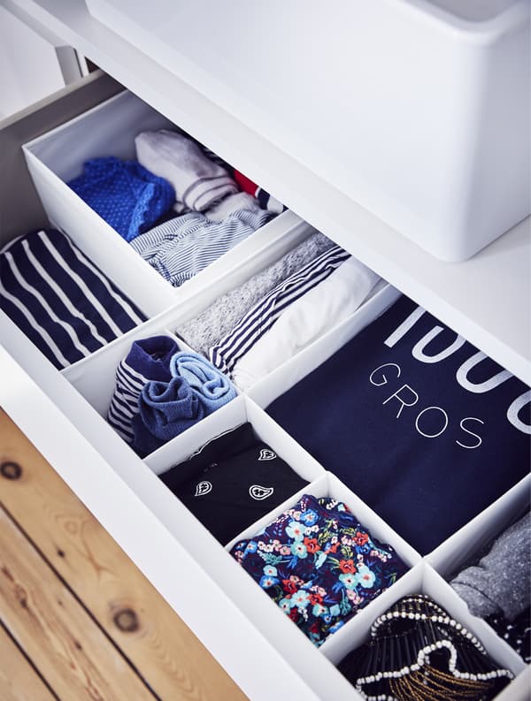 An open drawer with clothes in compartments.