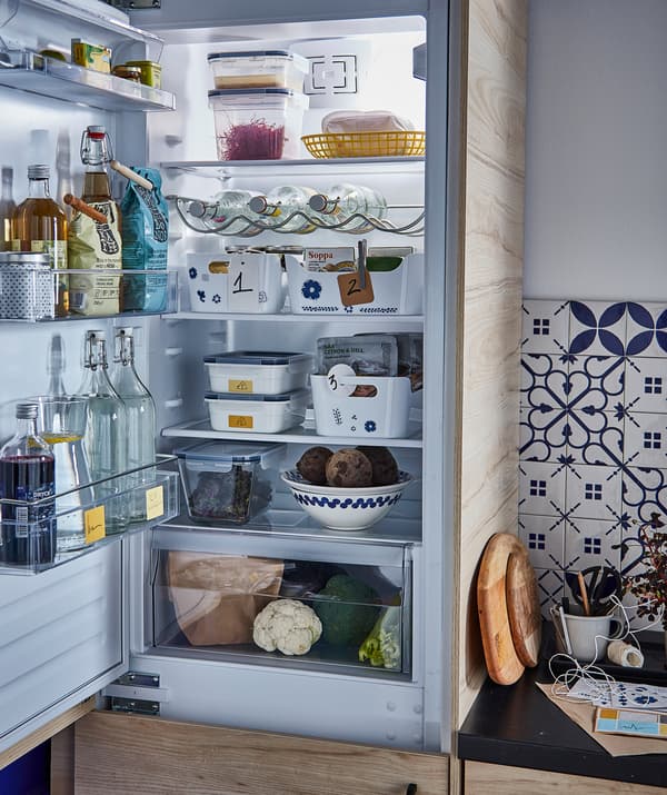 An open fridge filled with food and drink: bottles in the door, containers on the shelves, drawer for vegetables at bottom.