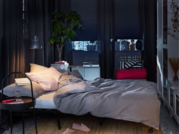 An open IKEA LYCKSELE sofa bed, with grey bedding, dark grey curtains and block out blinds.