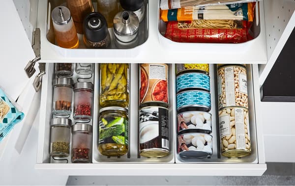 An open IKEA MAXIMERA white kitchen pantry drawer displaying organized cans, spices and oils.