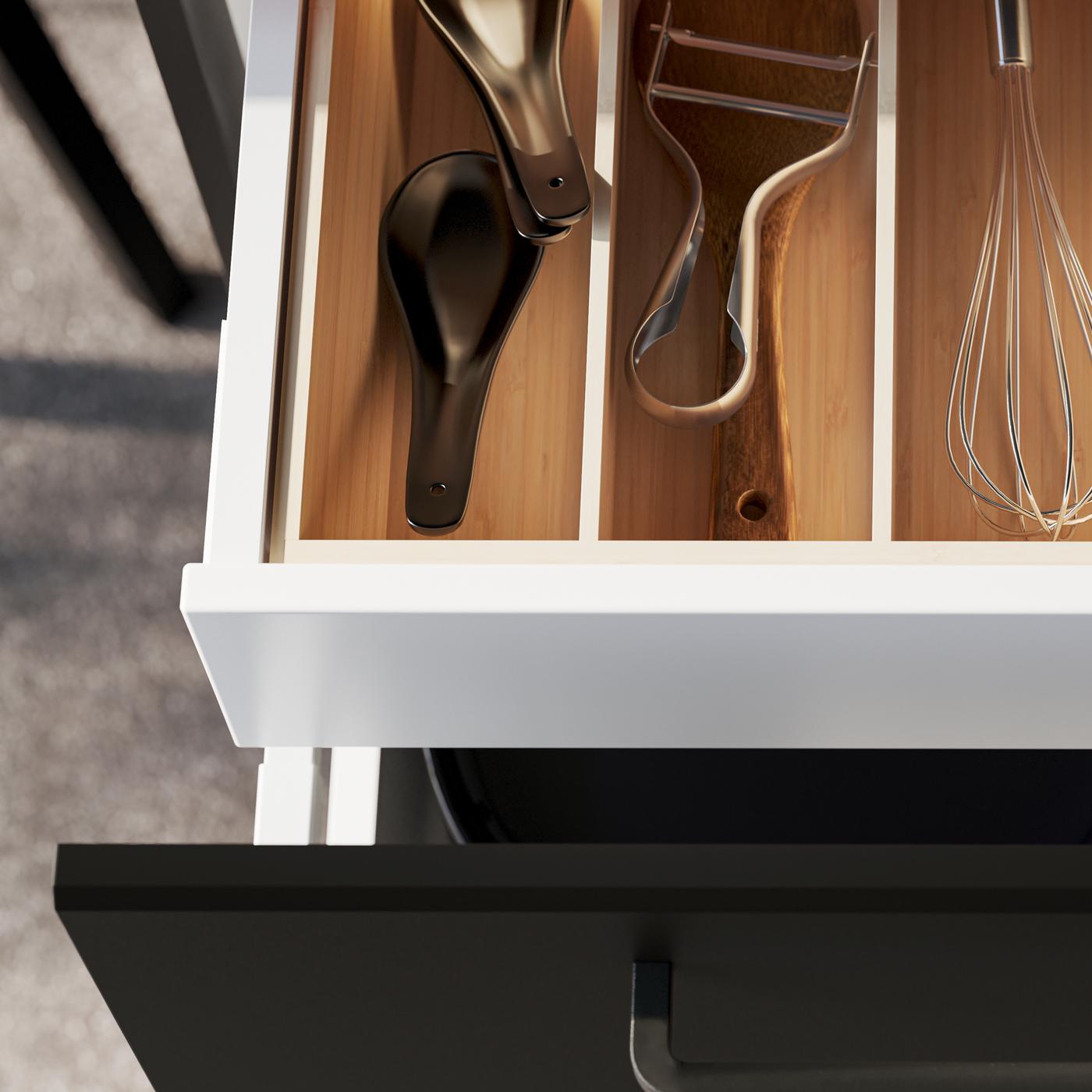 An open kitchen drawer with a black front, revealing kitchen utensils inside an UPPDATERA cutlery tray in light bamboo.