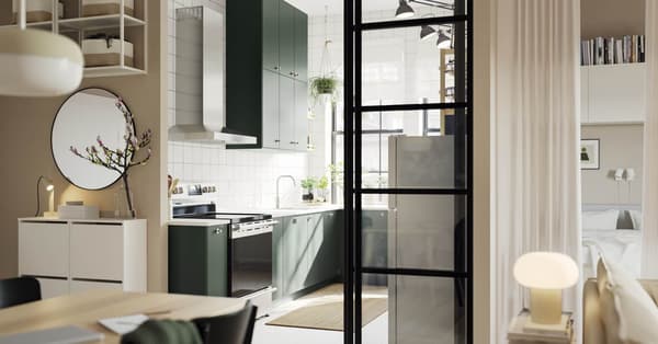 An open kitchen with deep green HAVSTORP kitchen fronts and wall cabinets up to the ceiling, next to a bright living room.